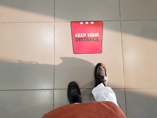 在新冠肺炎疫情期间，一名男子站在餐馆和商店瓷砖地板上的社交距离标记上。图片下载