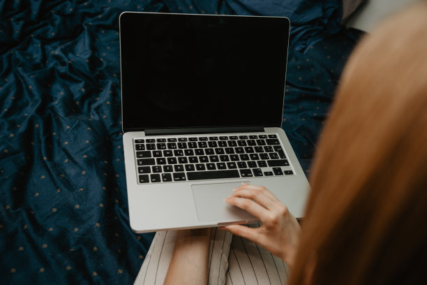 一个女人坐在舒适的床上用笔记本电脑工作的俯视图，一个黑屏图片下载