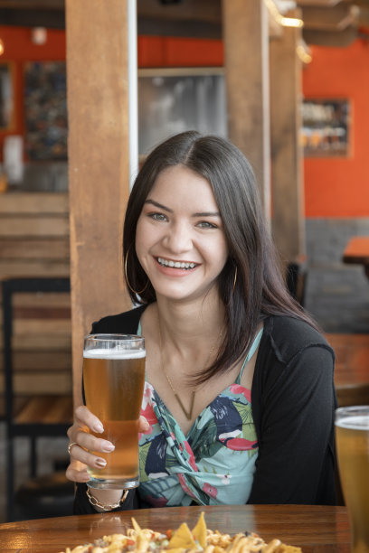 开朗美丽的长发女子坐在餐厅用木制家具坐着，手里拿着一个水晶酒杯喝着酒，穿着休闲的衣服，生活方式图片下载