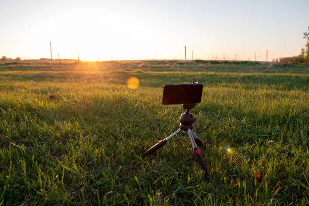三脚架上的智能手机在田野里捕捉日落图片下载