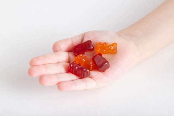 幼儿手握各色儿童维生素泰迪熊，白色背景，孤立。复合维生素图片下载