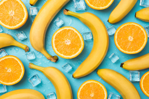 俯视图的照片冰块，水滴分散未剥皮的香蕉和切橙子在孤立的柔和的蓝色背景图片下载