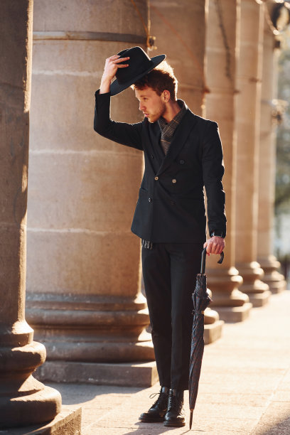 优雅的年轻人戴着黑帽子，穿着黑衣服，手里拿着雨伞在城外图片下载