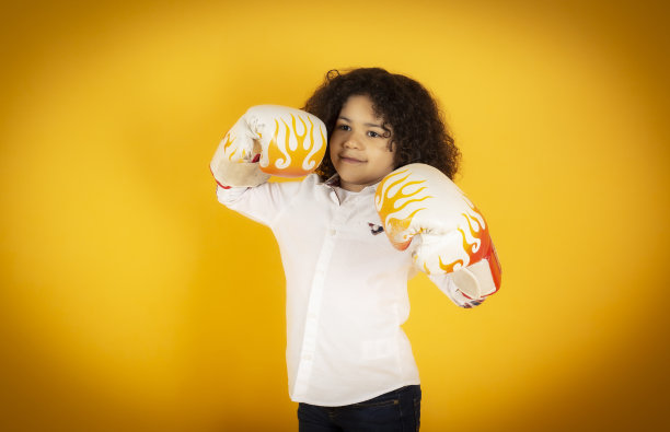 小男孩一头卷发，戴着黄色背景的拳击手套图片下载