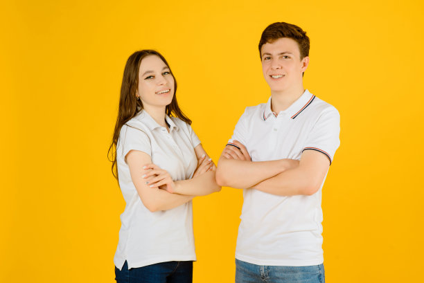 一对年轻幸福的男女穿着白色t恤，在黄色背景上笑着。图片下载