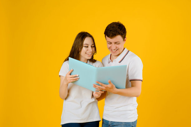 一对年轻幸福的夫妇的肖像，男人和女人穿着白色t恤正在读一本黄色背景的书。图片下载