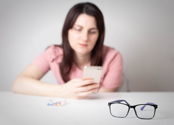 女孩看着智能手机的屏幕，眼镜在前景中。智能手机对人类视觉的危害图片下载