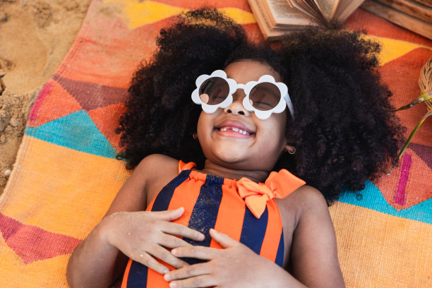 一个非洲裔美国女孩穿着鲜艳的泳衣在一个热带城市的海滩上晒太阳。夏天旅游的概念图片下载