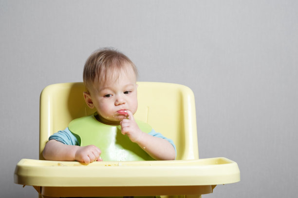 小孩子在灰色的背景上吃东西，孩子在思考，手指在嘴里图片下载