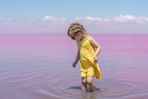 一个穿着黄色连衣裙的小女孩沿着粉红色的湖岸走着图片下载