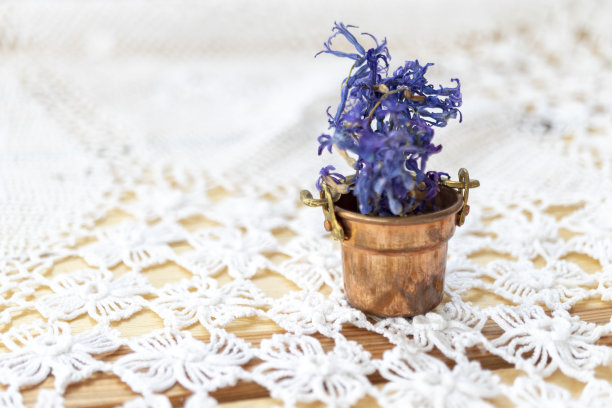 花边手工编织，桌布。在一张粉刷成白色的木桌上。上面有一个铜杯，里面装着干花。复古的照片。图片下载