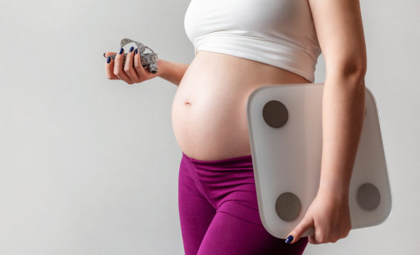 孕妇用卷尺测量她的腹部和体重秤。孤立在灰色背景。孕产妇新生儿健康、健康怀孕理念。图片下载