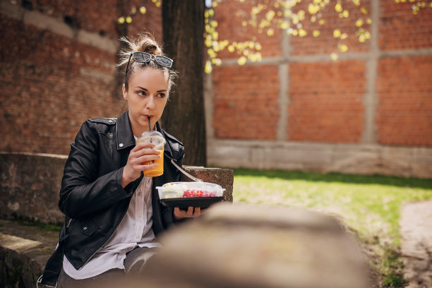 年轻女子在公园里吃着新鲜的有机沙拉，喝着橙汁图片下载