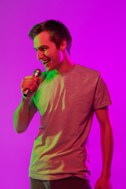 一个年轻的微笑的英俊的家伙与麦克风隔离在粉红色的霓虹灯背景。面部表情和人类情绪的概念图片下载