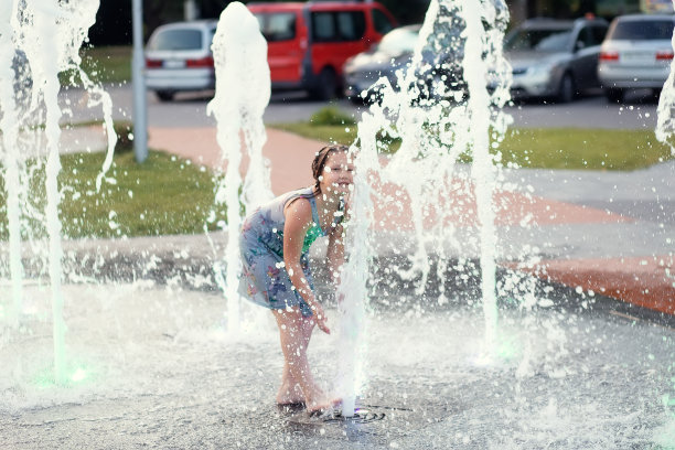 一个可爱有趣的小女孩在一个炎热的夏天在公共城市喷泉洗澡。孩子跑着，在水柱和水花间玩耍图片下载