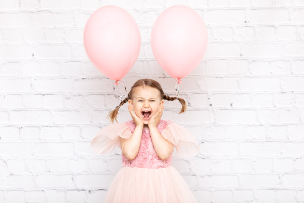 快乐的笑，令人惊讶的情绪，有趣的孩子女孩与淡粉色的气球靠近白色空砖墙工作室。孩子的生日聚会。广告气球。本空间图片下载