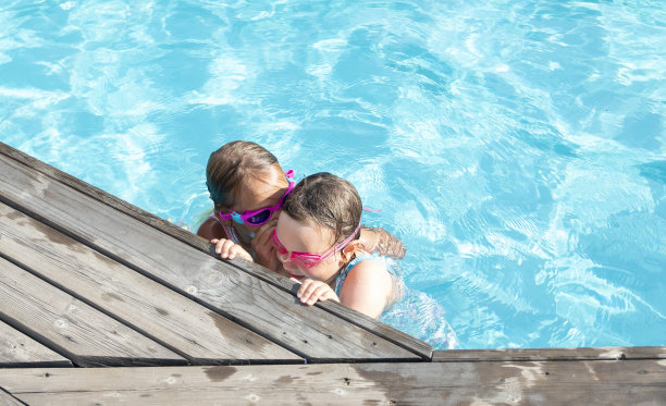 女孩，白种人的孩子，在室外游泳池游泳。两个朋友互相拥抱，低声耳语。图片下载