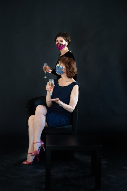两个戴面具的女人拿着一杯香槟，背景是黑色图片下载