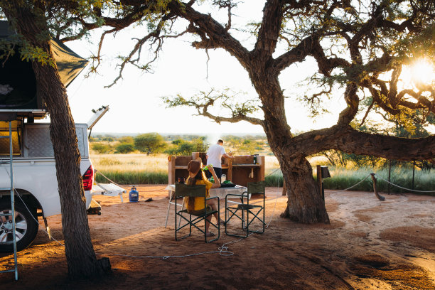 年轻的女人和男人露营与露营车在喀拉哈里沙漠享受日落和准备晚餐在纳米比亚库存照片图片下载