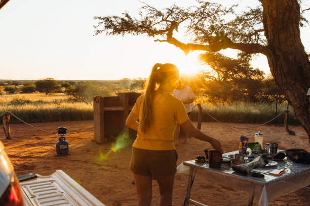 年轻的女人和男人露营与露营车在喀拉哈里沙漠享受日落和准备晚餐在纳米比亚库存照片图片下载