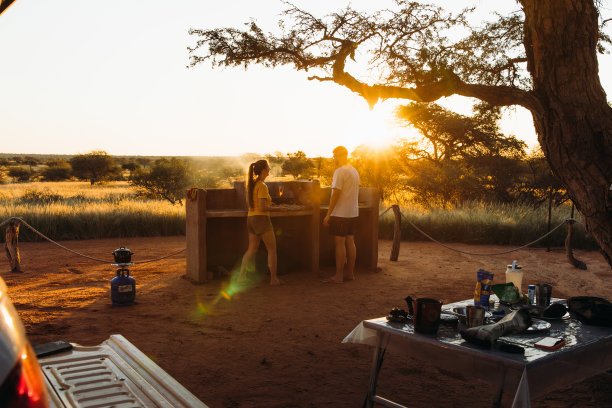 年轻的女人和男人露营与露营车在喀拉哈里沙漠享受日落和准备晚餐在纳米比亚库存照片图片下载