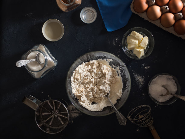 烹饪蛋糕。桌子上放着做馅饼的原料(面粉、鸡蛋、可可、黄油、糖、盐)、厨房用具和纺织品。从以上观点。平的。暗的背景图片下载