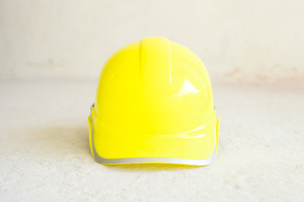 黄色的建筑工人。建筑工人在水泥地面上戴安全帽，正面图片下载