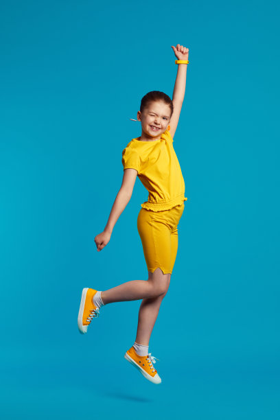 穿黄色衣服的女孩微笑着举起手，跳起来对抗蓝色图片下载