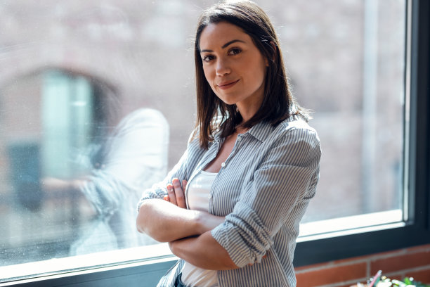 美丽的年轻女子看着相机，而站在客厅在家里。图片下载
