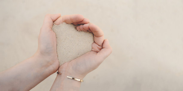 女人的手握着白沙滩上的细沙。图片下载