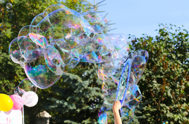 巨大明亮的肥皂泡映衬着天空和树木的背景。肥皂泡。夏季儿童活跃的休闲活动。图片下载