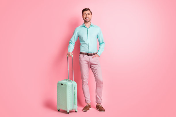 全身尺寸的照片，年轻男子保持行李在机场旅行的飞机上，在淡粉色背景孤立图片下载