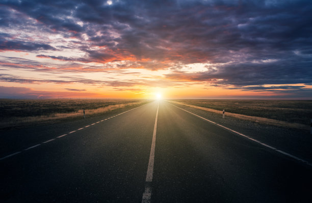 壮观的天空，多云的景色和夕阳在草原上公路被夕阳照亮图片下载