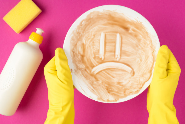 俯视图照片的手在黄色橡胶手套握着肮脏的盘子与画悲伤的脸黄色海绵和洗涤剂凝胶瓶没有标签在孤立的粉红色背景与copyspace图片下载