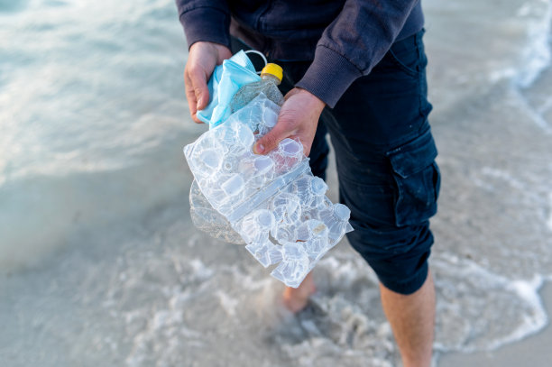 近距离拍摄，一个不认识的人拿着被大海回收的废物。塑料、口罩和瓶子垃圾。图片下载