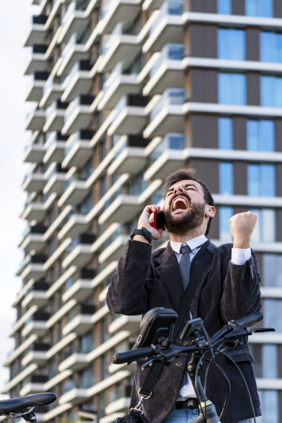 自信的年轻商人正在城市的街道上骑自行车和用手机聊天。图片下载