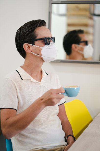 一名年轻男性顾客戴着口罩坐在现代咖啡店的桌旁图片下载