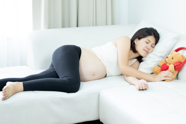 年轻漂亮的孕妇正在休息，睡在她家的沙发上。图片下载