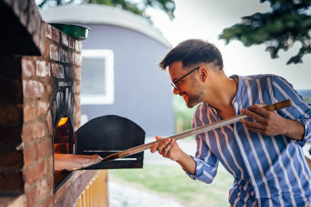 一个成年人，小心翼翼地把披萨放进烤箱。图片下载
