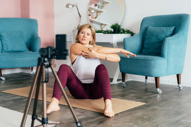 柔韧有吸引力的运动女性做体操在电话和录像前。图片下载