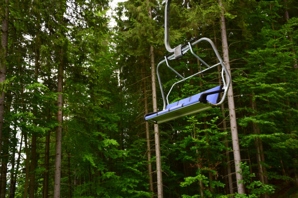 蓝色滑雪缆车上的一条空长凳从山上向下延伸，映衬着森林中的树木。这张照片摄于一个滑雪胜地的夏天图片下载