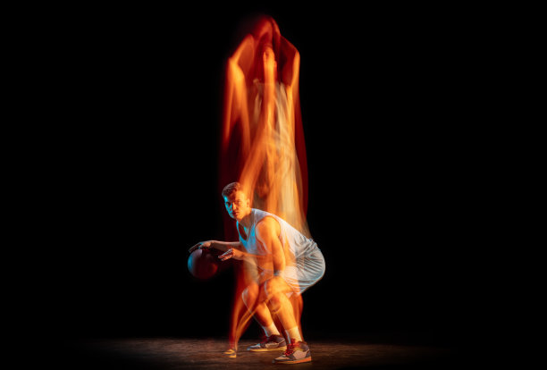 年轻的白人男性篮球运动员打篮球孤立在黑暗的演播室背景在混合光。健康生活理念，职业运动，爱好。图片下载