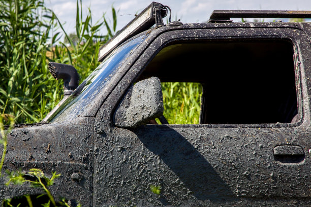 黑色SUV覆盖了一层沼泽脏车卡在芦苇丛的湖上去钓鱼主动休息和旅行通过自然保护区关闭驾驶门后镜，没有人。图片下载