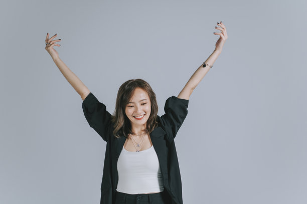 亚洲华人美丽的女子举起手臂微笑着与灰色的背景拍摄工作室图片下载