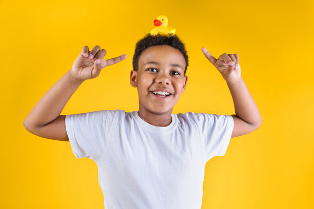 快乐的男孩在黄色的背景上拿着橡皮鸭的头图片下载