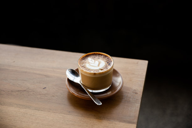一杯卡布奇诺，在茶碟上放着拉花，在木桌上放着勺子。图片下载