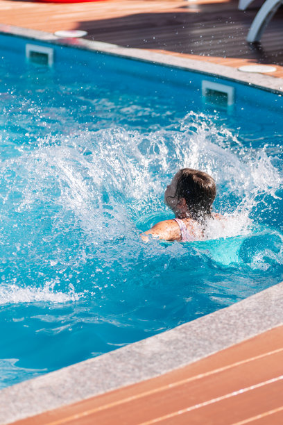 孩子们从泳池边跳进水里，溅起水花，享受着假期和炎热的夏天图片下载