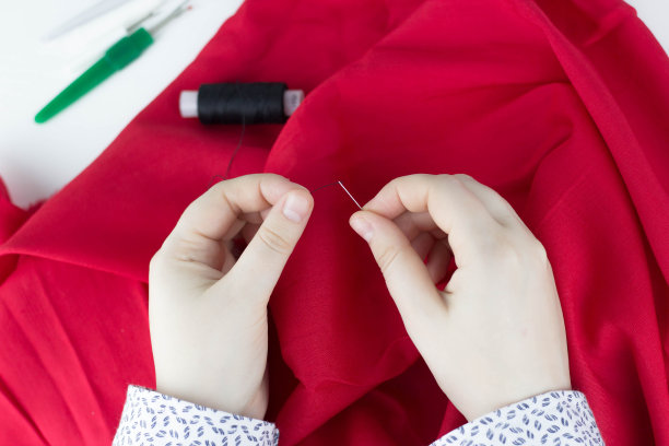 近距离观察缝纫过程。女性的手缝制红色织物。一个女孩手里拿着一根针。图片下载