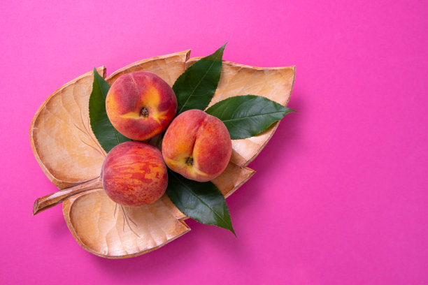 三个成熟的桃子在一个雕刻的木盘，绿色的树叶，特写图片下载