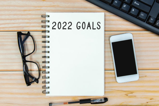 打开笔记本，上面写着“2022年目标”，木制背景上放着眼镜。图片下载